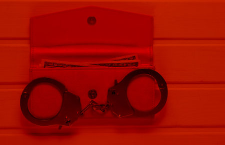 Steel handcuffs with open red leather wallet in red light. Theft, criminal concept.の写真素材