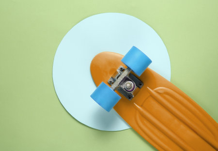 Cruiser board in the middle of green background with blue pastel circle. Youth hipster concept. Summer fun. Top viewの写真素材