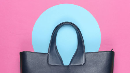 Fashionable leather bag on pink background with blue pastel circle. Top view