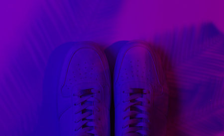 Stylish hister white sneakers on background with shadow from palm leaves. Neon gradient light. Top viewの写真素材