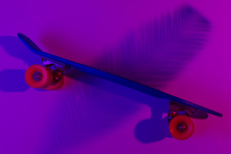 Plastic mini cruiser board on background with shadow from palm leaves. Neon gradient ligh. Top viewの写真素材