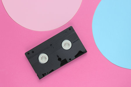 Video cassette on pink background with blue pink pastel circle for copy space. Top view. Minimalistic retro concept. 80s.の写真素材