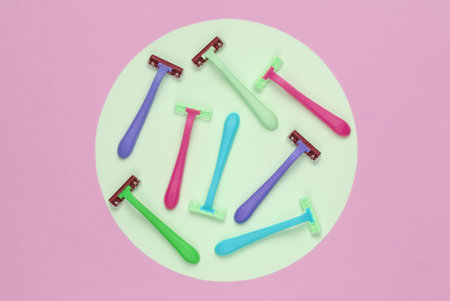 Many colored plastic razors on pink background with green pastel circle. Minimalistic beauty still lifeの写真素材