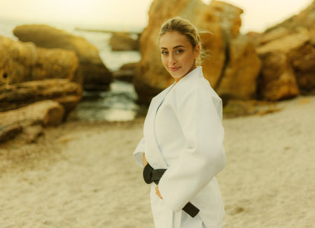 Portrait of young attractive martial arts master woman in white kimono with black belt on wild beachの写真素材
