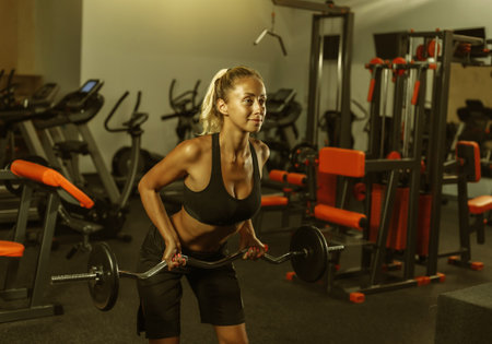 Young fit woman in sportswear is training with a barbell in the gym. Healthy lifestyle concept. Body...