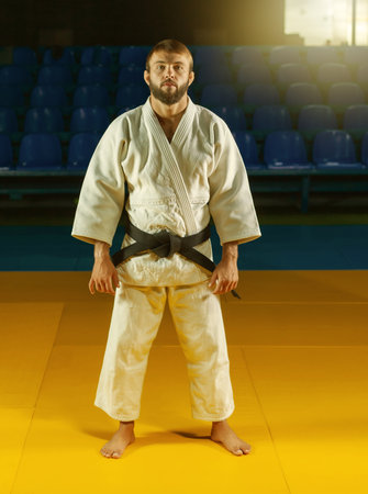Portrait of martial artist in white kimono with black belt in sport hall