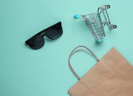 Minimalism shopping concept. Paper shopping bag, mini shopping cart and sunglasses on blue background. Top viewの写真素材