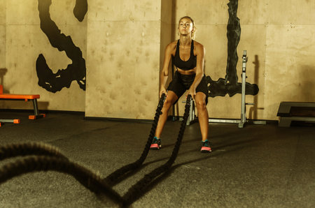 Young sport woman in sportswear is training with battle rope in the gym. Functional training....