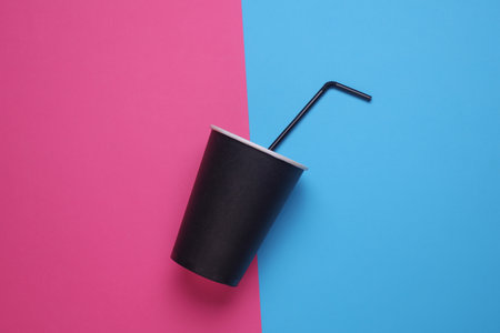 Black disposable cup for hot drinks with straw on pink blue backgroundの写真素材