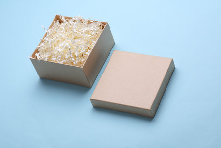 Open Kraft cardboard box with paper filler on blue background