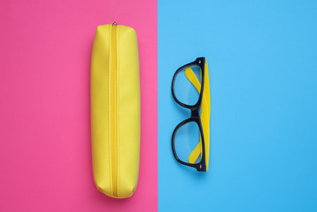 Yellow pencil case with eyeglasses on pink blue background. Flat layの写真素材