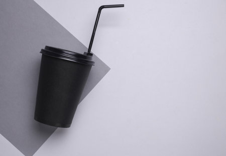 Black disposable cup for hot drinks with straw and lid on gray backgroundの写真素材