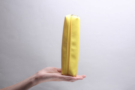 Hand holding yellow pencil case on gray backgroundの写真素材