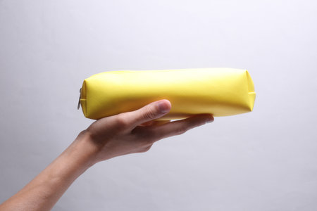 Hand holding yellow pencil case on grey backgroundの写真素材