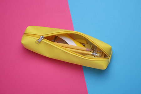 Yellow pencil case with stationery on pink blue background. Flat layの写真素材