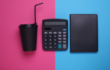 Black disposable cup for hot drinks and notebook, calculator on pink blue background. Flat layの写真素材