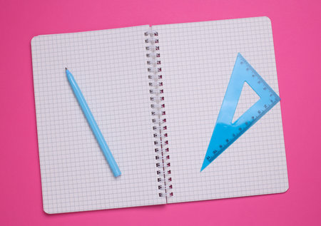 Notebook with triangle ruler and pen on pink background