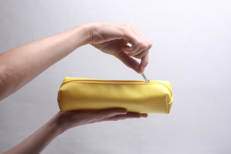 Hand holding yellow pencil case on grey backgroundの写真素材
