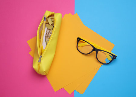 Yellow pencil case with stationery on pink blue background. Flat layの写真素材
