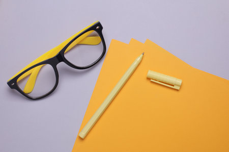 Yellow sheets of paper with eyeglasses and stationery on gray backgroundの写真素材