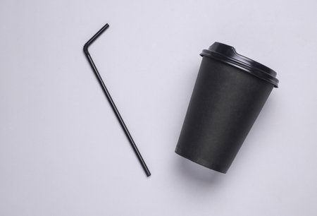 Black disposable cup for hot drinks with straw and lid on gray backgroundの写真素材