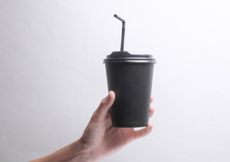 Hand holding Black disposable cup for hot drinks with straw and lid on gray backgroundの写真素材