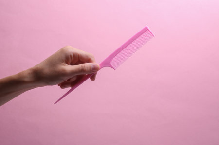 Female hand holding plastic comb on pink backgroundの写真素材