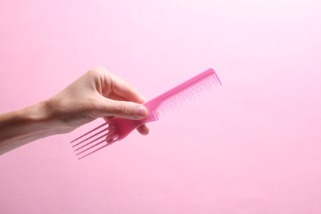 Female hand holding plastic comb on pink backgroundの写真素材