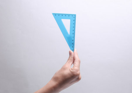 Hand holding a triangular ruler on a gray backgroundの写真素材