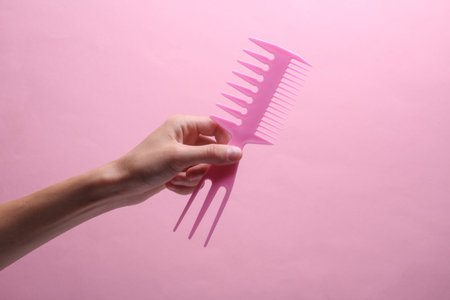 Female hand holding plastic comb on pink backgroundの写真素材