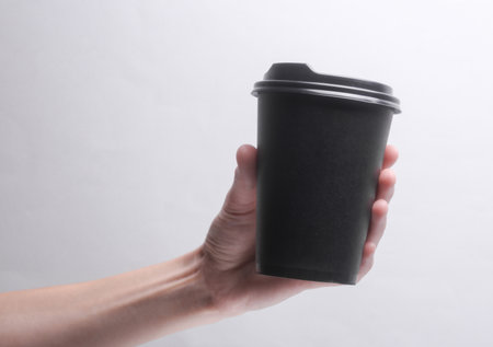 Hand holding Black disposable cup for hot drinks with lid on gray background