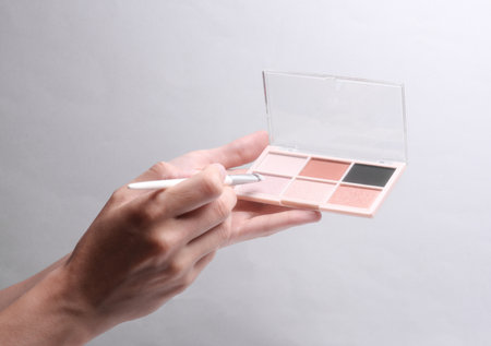 Female hands holding makeup palette with brush on gray backgroundの写真素材