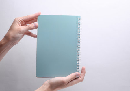 Female hands holding spiral notebook on gray backgroundの写真素材