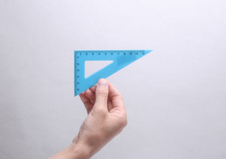 Hand holding a triangular ruler on a gray backgroundの写真素材