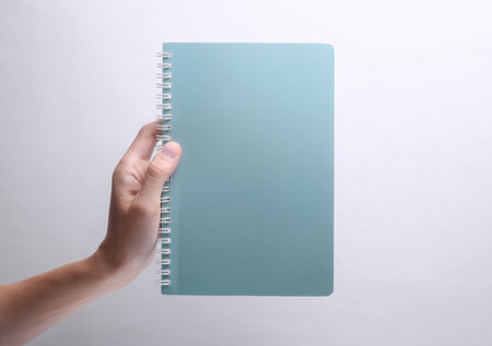 Female hand holding spiral notebook on gray backgroundの写真素材
