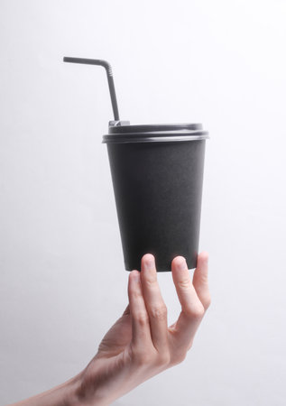 Hand holding Black disposable cup for hot drinks with straw and lid on gray backgroundの写真素材