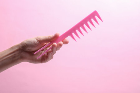 Female hand holding plastic comb on pink backgroundの写真素材
