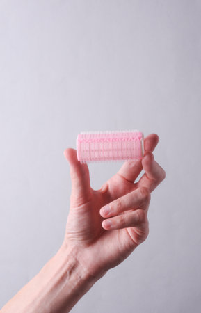 Female hand holding plastic curlers on gray backgroundの写真素材