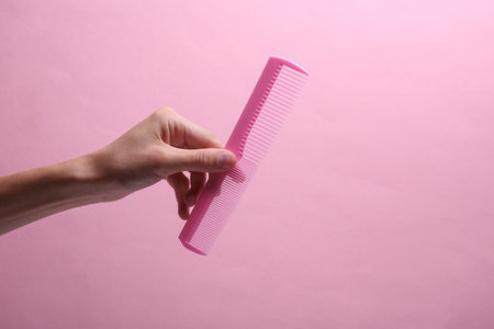Female hand holding plastic comb on pink backgroundの写真素材