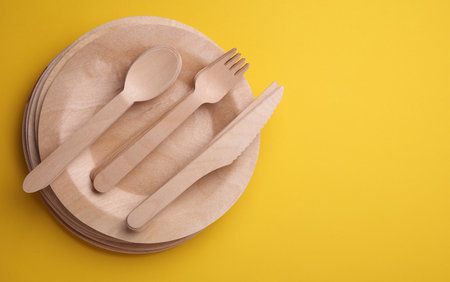 Set of wooden eco dishes on yellow background. Plates, forks, knives and spoonsの写真素材