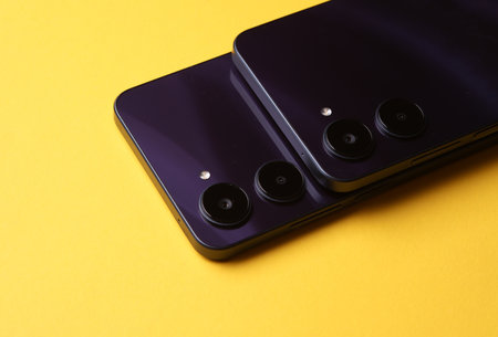 Two modern smartphones with dual camera, view from the back cover. Yellow backgroundの写真素材