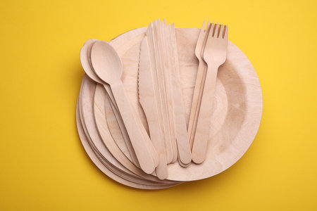 Set of wooden eco dishes on yellow background. Plates, forks, knives and spoonsの写真素材