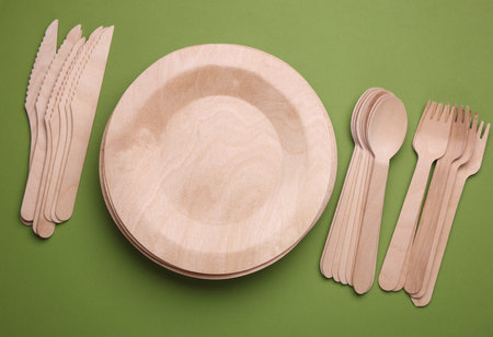 Set of wooden eco dishes on green background. Plates, forks, knives and spoonsの写真素材