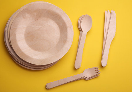 Set of wooden eco dishes on yellow background. Plates, forks, knives and spoonsの写真素材