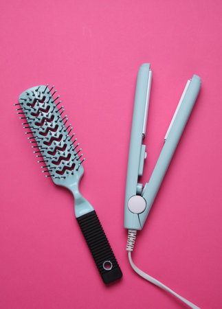 Hair straightener and hairbrush on pink backgroundの写真素材