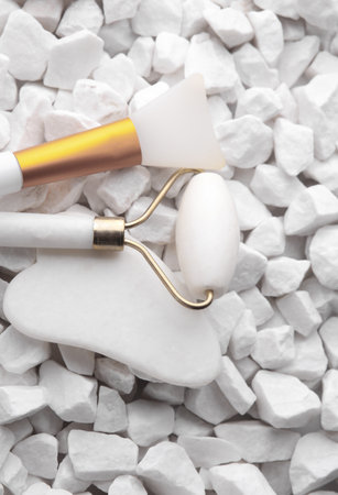 Jade roller and gua sha facial scraper on white pebblesの写真素材