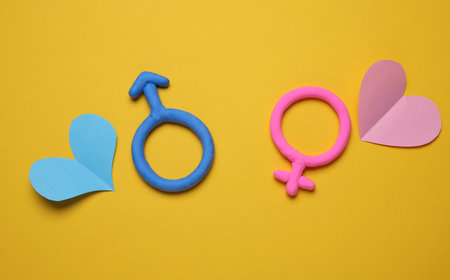 Male and female gender symbols made of plasticine with hearts on yellow backgroundの写真素材