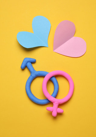 Male and female gender symbols made of plasticine with hearts on yellow backgroundの写真素材