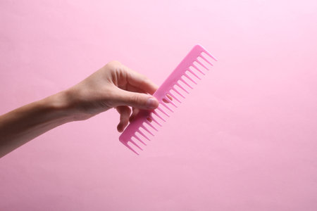 Female hand holding plastic comb on pink backgroundの写真素材