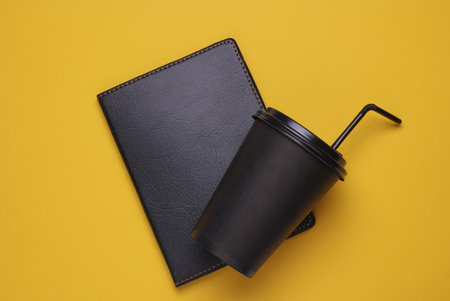 Black disposable cup for hot drinks and notebook on yellow backgroundの写真素材